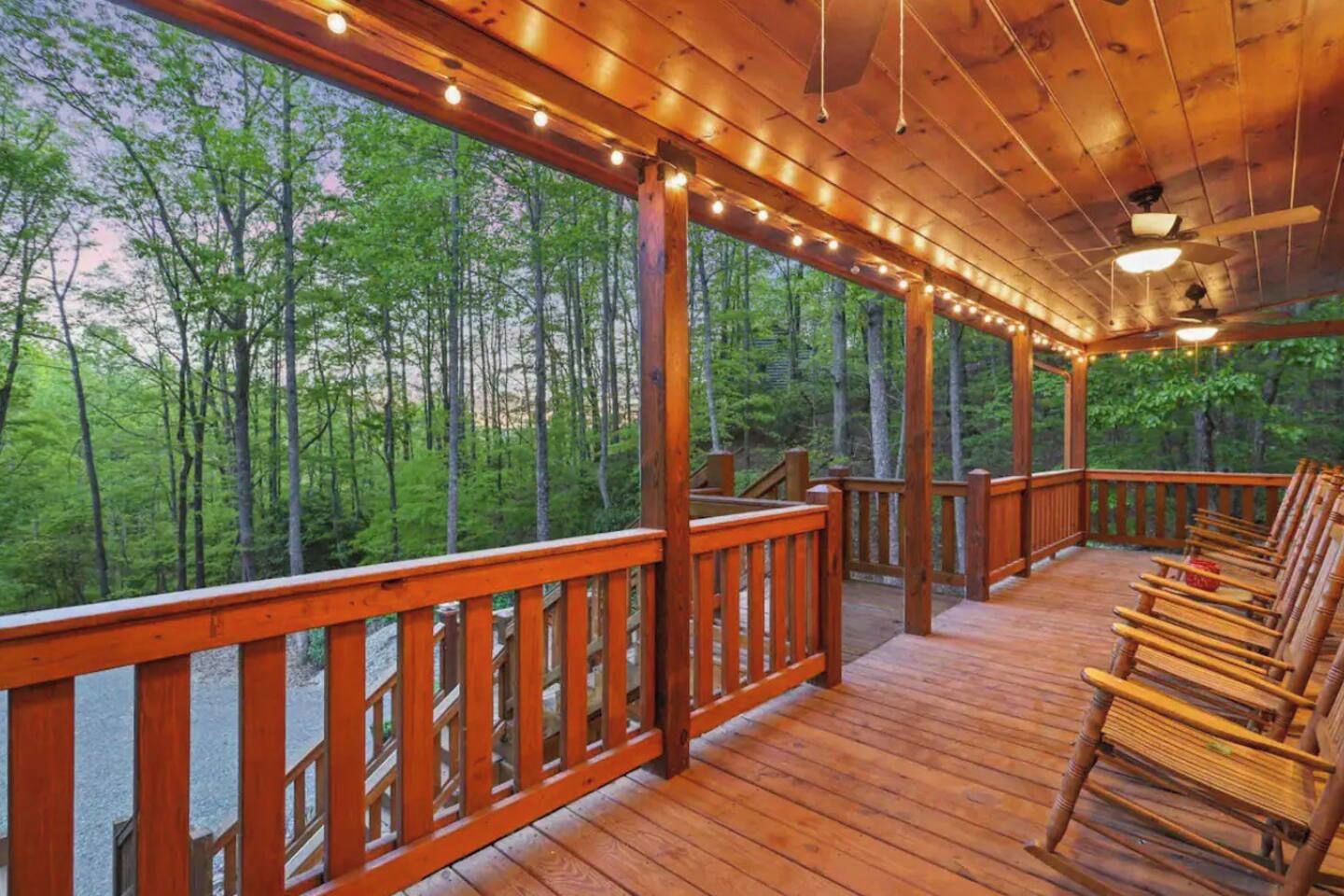 Una terraza de madera con barandilla, rodeada de árboles y amueblada con sillas de madera.