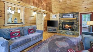 A wooden cabin interior with a sofa, television, fireplace, and ceiling fan. - Upscale Morganton Cabin w/ Hot Tub & Arcade (Morganton)
