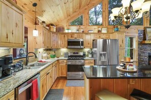 A kitchen with wooden cabinets, stainless steel appliances, granite countertops, and a chandelier.
