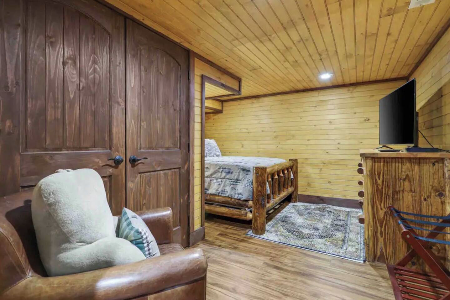 A wooden room with a bed, a TV, and a leather chair.