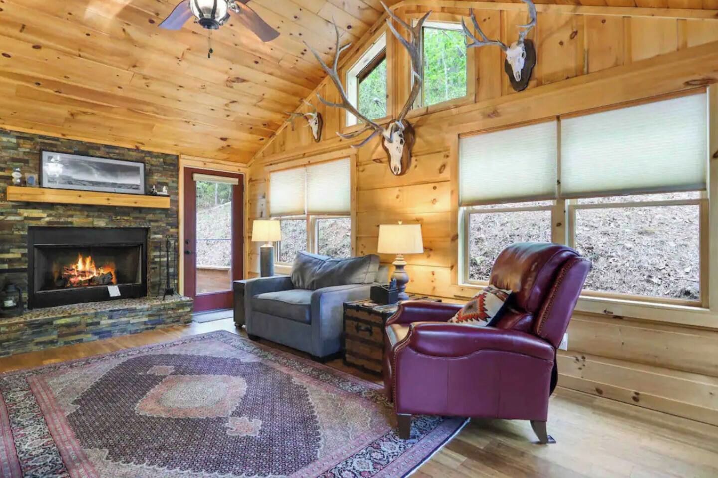 A log cabin interior with a fireplace, leather sofa, and a large rug.