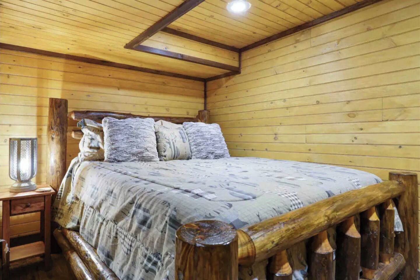 Habitació de fusta amb un llit, una tauleta de nit i un calefactor fixat a la paret.