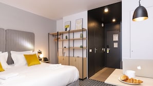 Une chambre d’hôtel avec un lit, un bureau avec un ordinateur portable et un croissant, une armoire et une porte avec une pancarte.