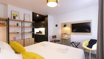 A hotel room with a large bed, a desk with a chair, a TV, and a shelf with towels.
