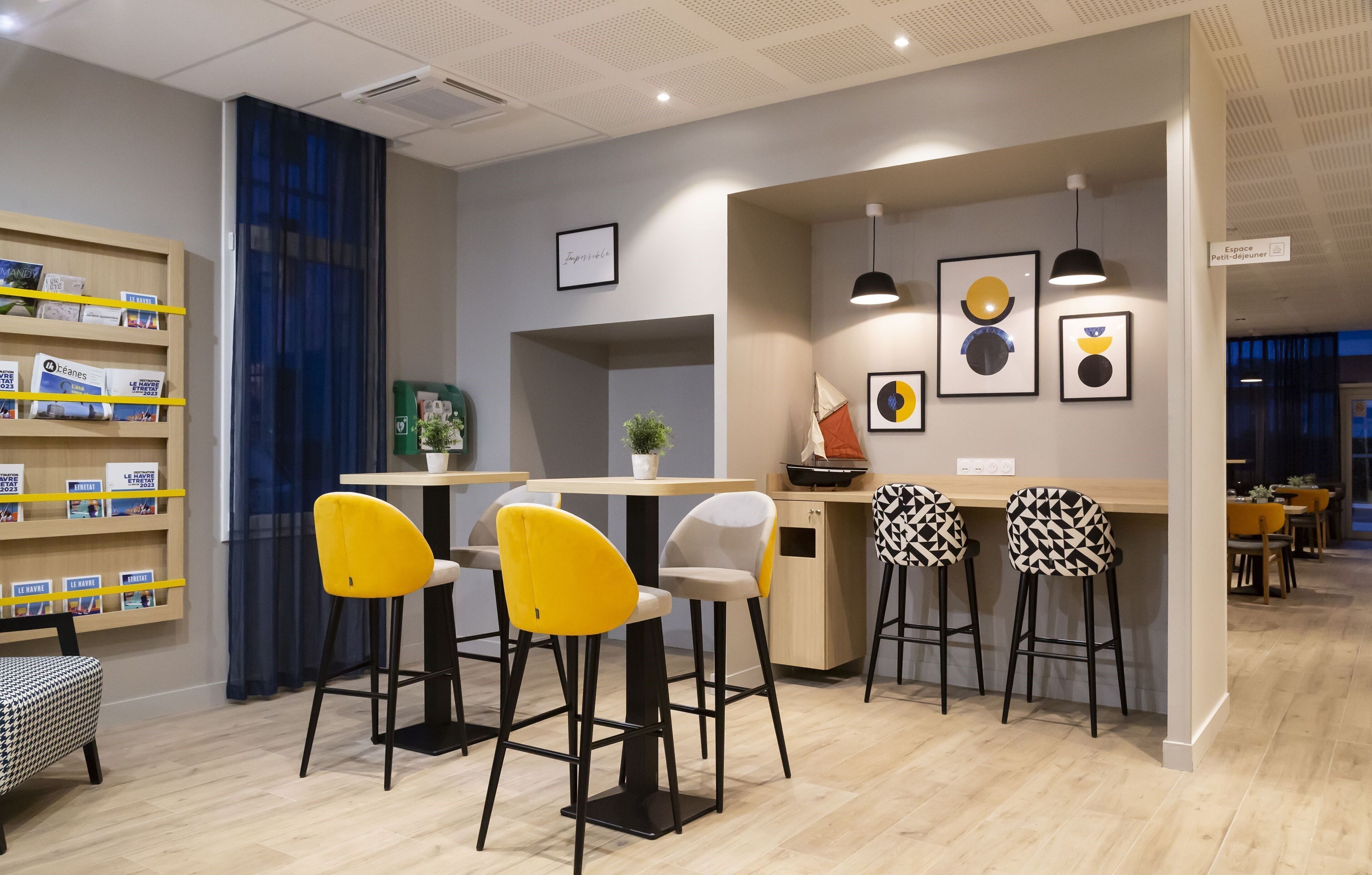 A modern bar area with yellow and black patterned stools, a bookshelf with magazines, and framed artwork on the wall.