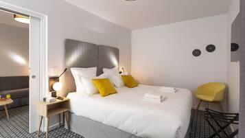 Une chambre d’hôtel avec un grand lit, des tables de chevet, une chaise et un canapé dans la pièce adjacente.