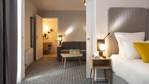 Habitación de hotel con cama, escritorio con computadora portátil, sofá y baño visible a través de una puerta abierta.