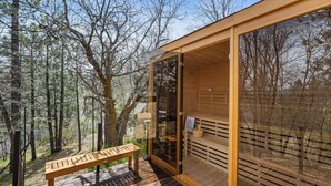 Una sauna in legno con porte in vetro, una panca di legno e una terrazza circondata da alberi.