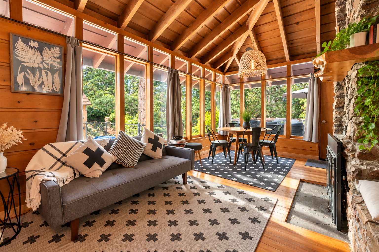 A cozy room with a sofa, dining table, and chairs, large windows, and a stone wall.