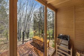 Una cabaña de madera con terraza, una mesa y una parrilla.