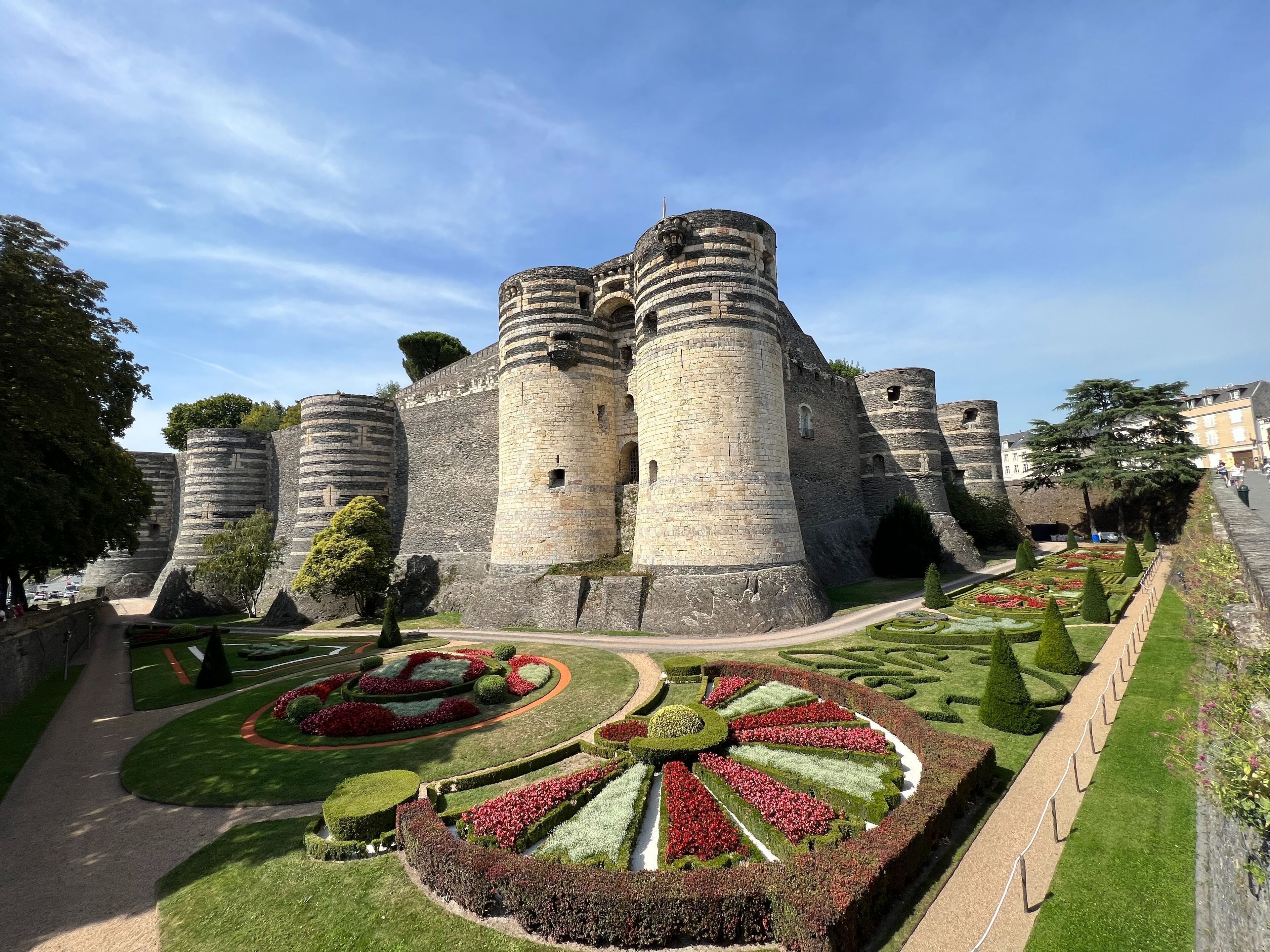 Un castillo histórico con numerosas torres de piedra y un jardín bien cuidado con parterres geométricos.