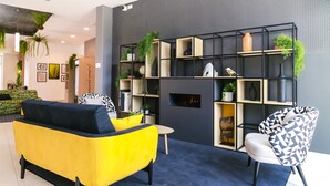 Ein modernes Wohnzimmer mit einem gelben Sofa, einem gemusterten Sessel, einem Kamin und einem schwarz-weißen Bücherregal.