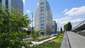 Ein modernes Gebäude mit einem markanten, winkelförmigen Design, umgeben von Grünflächen und einem Fußweg.