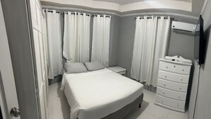 A bedroom with a bed, nightstand, dresser, and a wall-mounted TV. - Home Away From home. (Bridgetown)