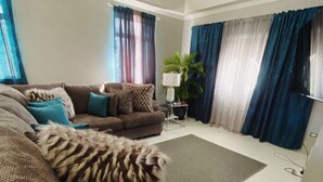A living room with a brown sofa, teal cushions, a green rug, and a potted plant. - Home Away From home. (Bridgetown)