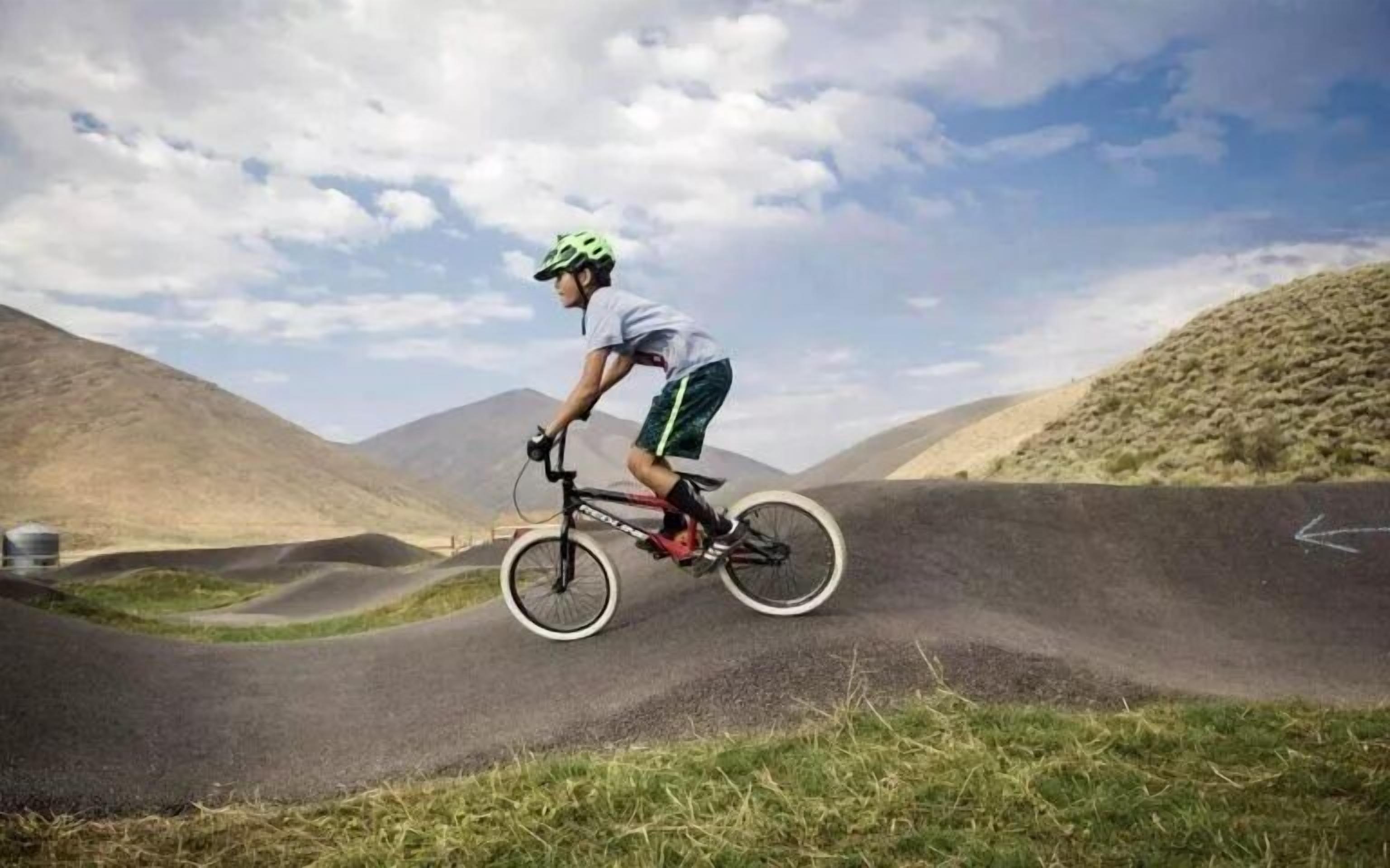 A person riding a bicycle on a track with hills in the background.