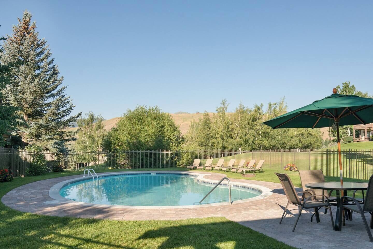 A swimming pool with a surrounding deck, lounge chairs, and a table with chairs.