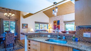 Eine moderne Küche mit Granit-Arbeitsplatten, Holzschränken und einer integrierten Spüle. Es gibt eine Essecke mit einem Stuhl in ZEBRA-Optik sowie einen Tisch und ein großes Fenster, das für natürliches Licht sorgt.