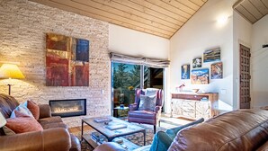 Ein gemütliches Wohnzimmer mit Steinwand, Ledermöbeln, Kamin und Blick durch große Fenster.