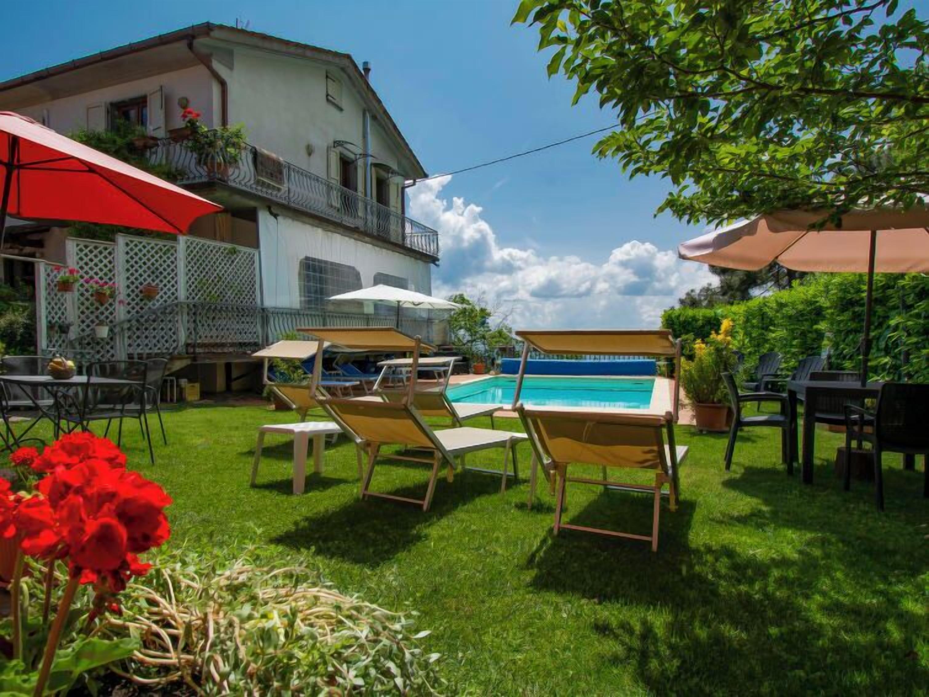 A poolside area with lounge chairs and umbrellas, a pool, and a building with a balcony.