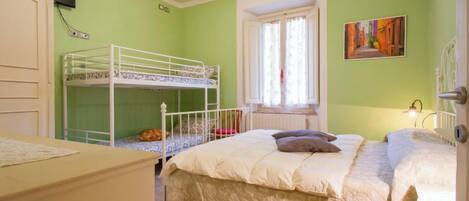 Une chambre avec des lits superposés, une fenêtre avec des rideaux, un radiateur et un tableau accroché au mur.