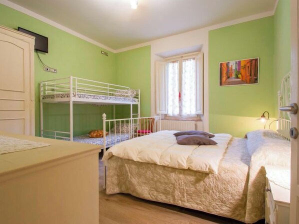 Una habitación con literas, una ventana con cortinas, un radiador y un cuadro en la pared.