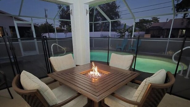 Een overdekt terras met een houten tafel en stoelen, een vuurplaats en uitzicht op een zwembad.
