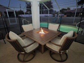 A covered patio with a wooden table and chairs, a fire feature, and a view of a swimming pool. - Heated Pool & Firepit, Peaceful and Serene - Villa Colada Cove - Roelens Vacations (Cape Coral)