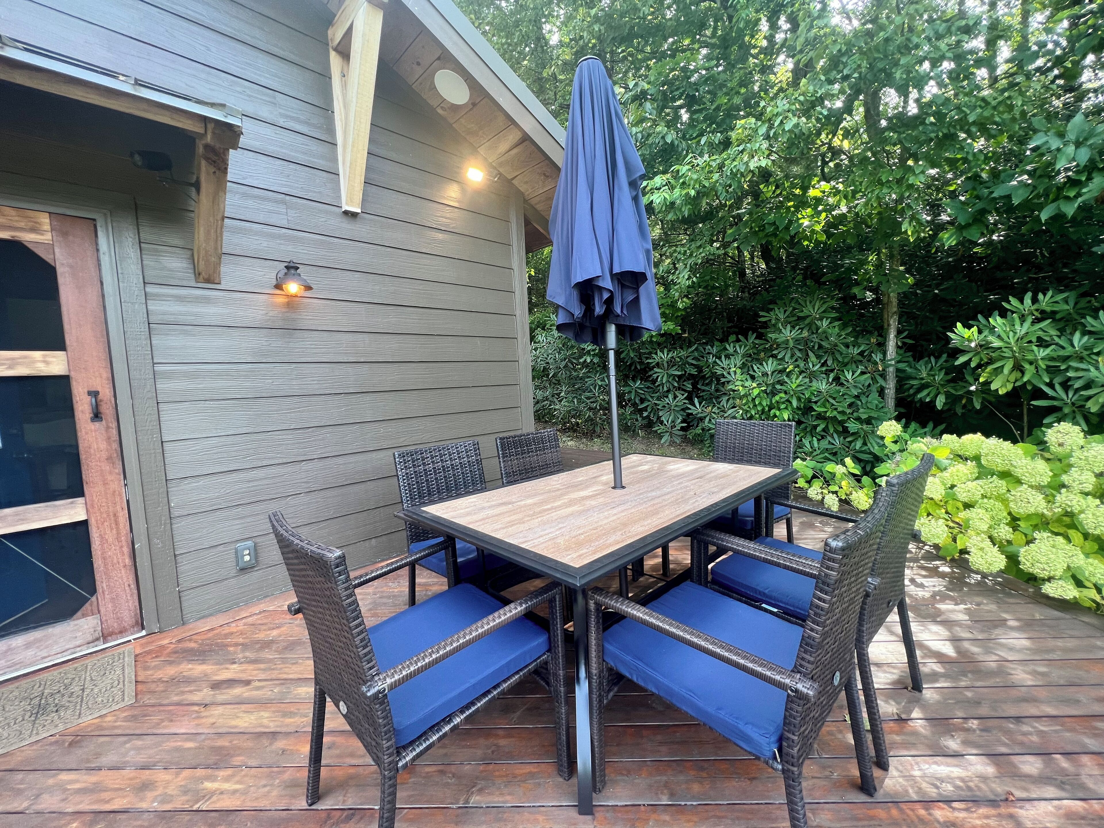 Eine Holzterrasse mit Tisch und Stühlen, umgeben von Grünpflanzen.