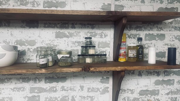 A kitchen shelf with jars of spices, a bottle of cooking spray, and a white candle.