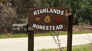A wooden sign with the text "HIGHLANDS HOMESTEAD" and symbols of a pig, a beehive, and a rooster.