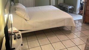 A bedroom with a bed, a ceiling fan, an air conditioning unit, a door, and a window with curtains.