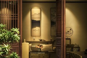 A traditional room with a wooden door, a sofa with cushions, a small table with a vase of flowers, and wall-mounted artwork. - First Sight Boutique Cottage (Tengchong)