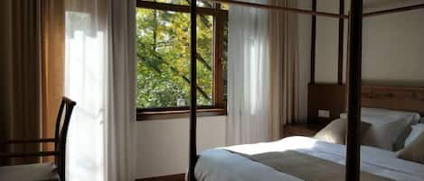Un lit à baldaquin avec un cadre en bois, une chaise et une fenêtre avec des rideaux.