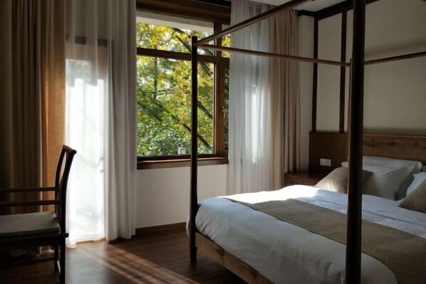 A four-poster bed with a wooden frame, a chair, and a window with curtains.