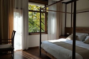 Una cama con dosel de madera, una silla y una ventana con cortinas.