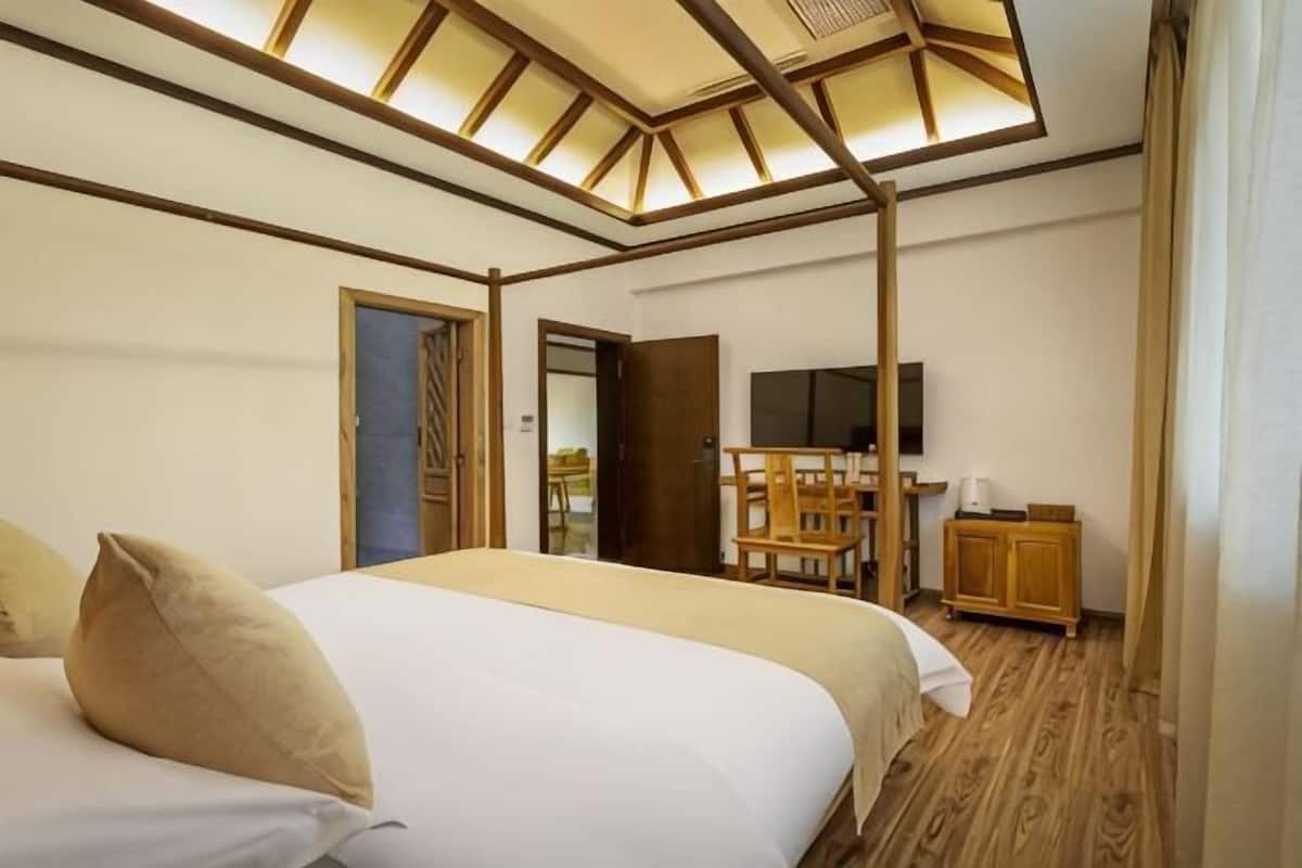 A bedroom with a bed, wooden flooring, a TV, and a desk with a chair.