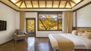 A bedroom with a large bed, a chair, a TV, and a window with a view of trees. - First Sight Boutique Cottage (Tengchong)
