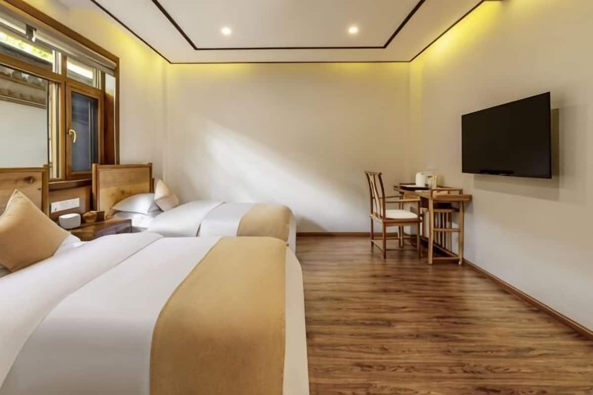 A hotel room with two beds, a desk, a chair, and a TV mounted on the wall.