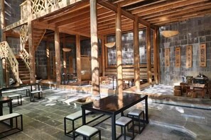 Un'ampia area interna con travi in legno, pavimento in pietra e un tavolo centrale con panche.