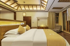 A hotel room with a large bed, a bedside table, a mirror, a chair, and a bathroom with a shower and toilet. - First Sight Boutique Cottage (Tengchong)