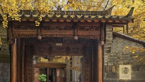 A traditional wooden gate with intricate carvings, a stone wall, and a sign with Chinese characters. - First Sight Boutique Cottage (Tengchong)