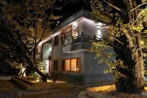 Un edificio de dos pisos con balcón, rodeado de árboles e iluminado con luz artificial.
