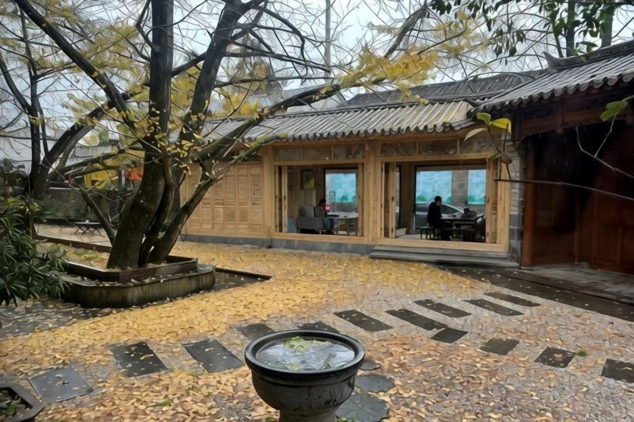 A traditional building with a tiled courtyard, a large tree, and a water feature.