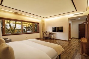 A bedroom with a large bed, a desk, a chair, a TV, and a window with a view of trees. - First Sight Boutique Cottage (Tengchong)