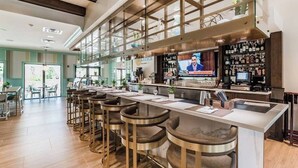 Eine moderne Bar mit einer langen Theke, mehreren Barhocker und einem Fernsehbildschirm, der eine Nachrichtensendung zeigt.
