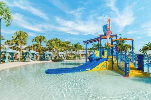 A water park with a blue and yellow water slide, surrounded by palm trees and lounge chairs.
