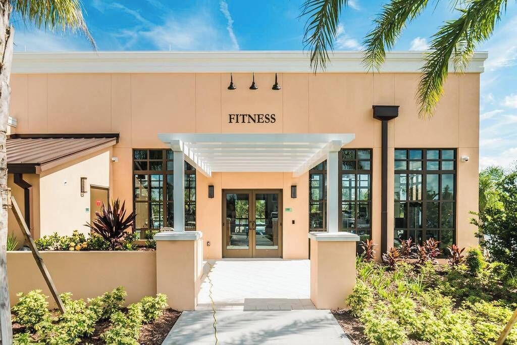 Un bâtiment moderne avec une enseigne « FITNESS » au-dessus de l’entrée, doté d’une passerelle couverte et de portes en verre.