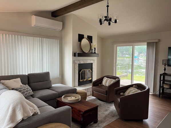 Una sala de estar con un sofá modular, dos sillones, una chimenea y un ventanal con vista a un cuerpo de agua.