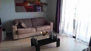 Una sala de estar con un sofá color beige, una mesa de centro de vidrio y un cuadro en la pared.